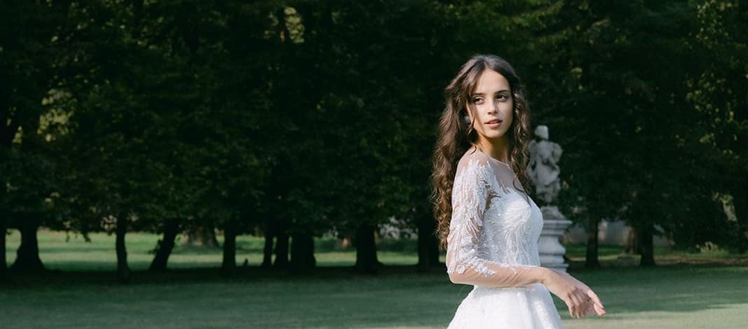 A bride in a lace gown turning in the grounds of a Riviera château, backlit by late afternoon sun.