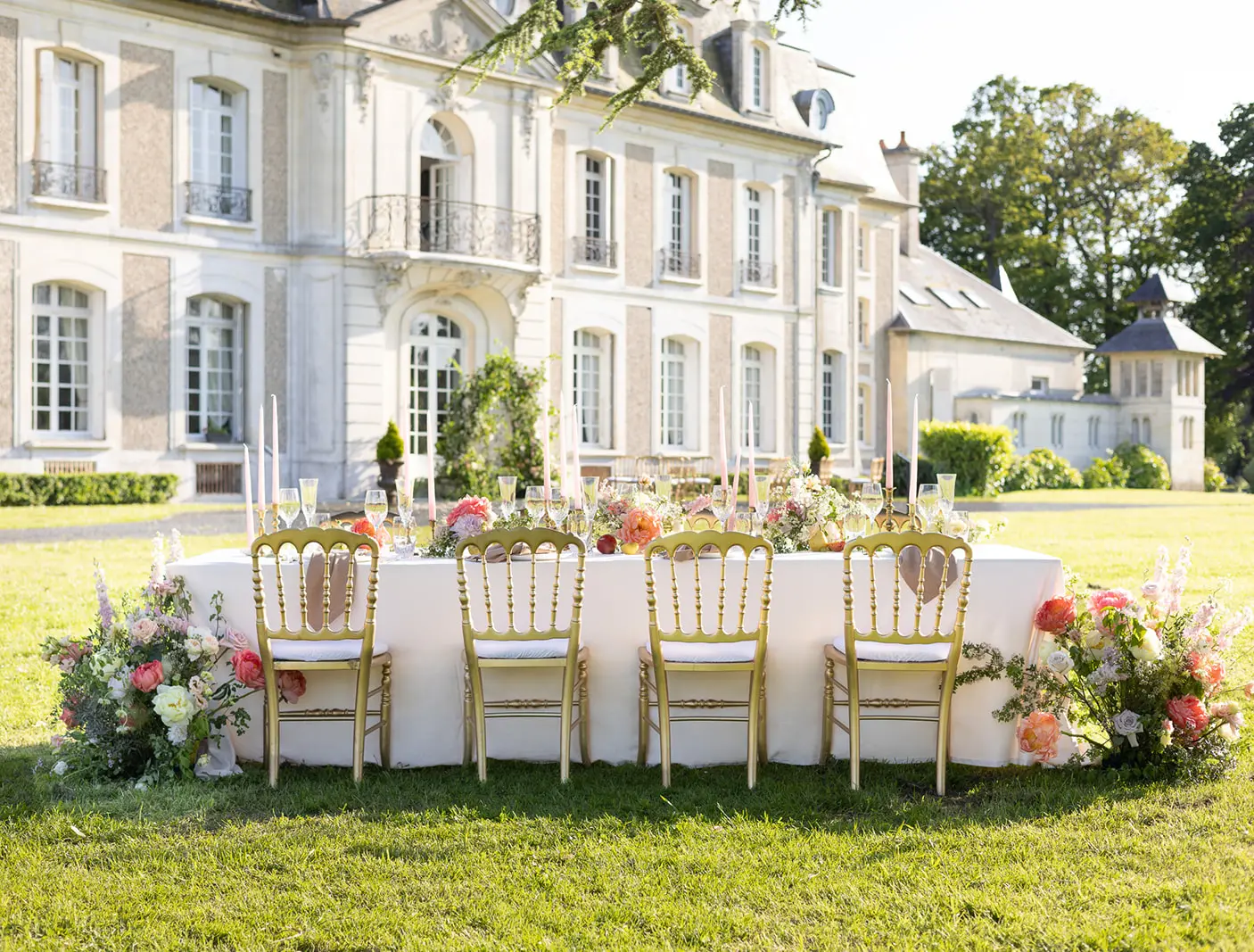 A long banquet table dressed in white and flowers on the lawn of a Riviera château, late afternoon.